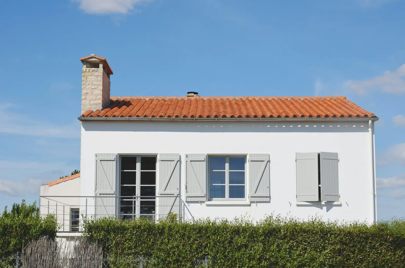 Maison aux murs blancs et à la toiture en tuiles rouges, volets gris